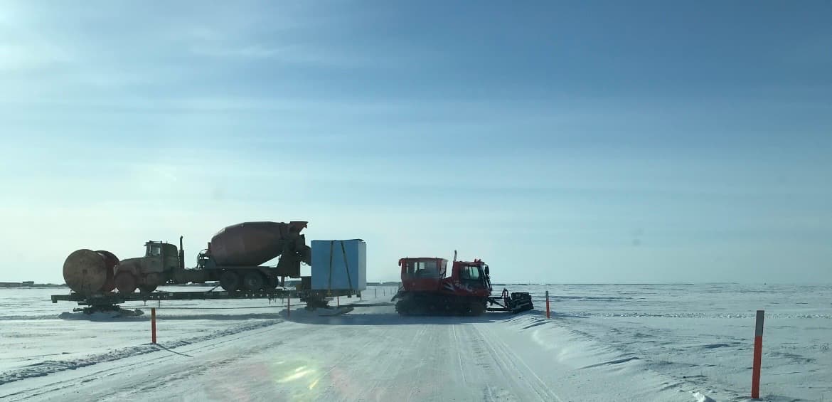 A cement truck on a sled pulled across an open ice road.