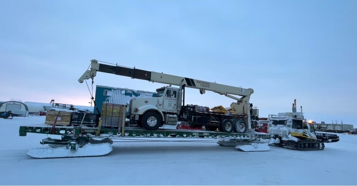 A Peterbilt picker truck loaded on a Mammoth sled at arctic twilight.