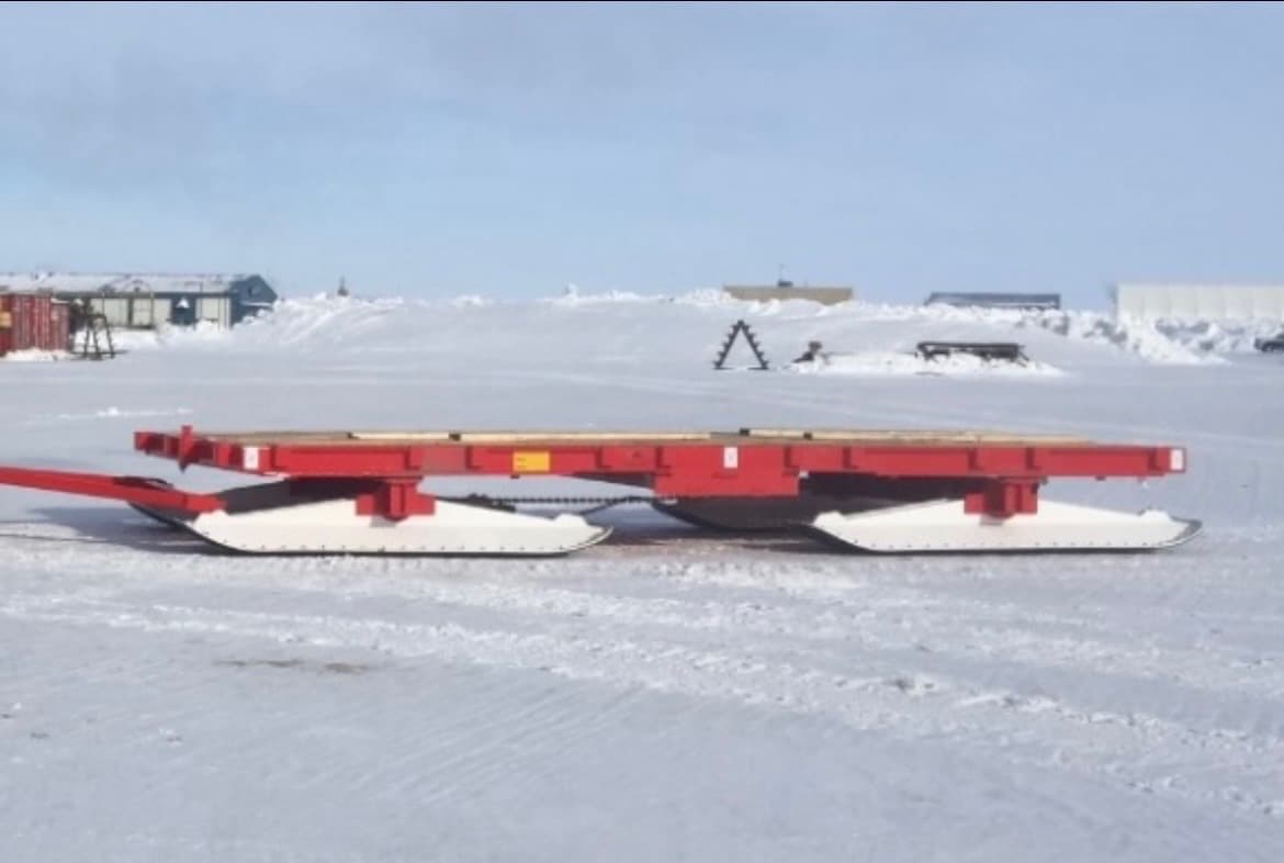 Empty Mastodon sled in profile on snow, red deck and white runners.